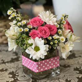 Pink roses and white daisies arranged in a glass vase with a pink polka-dot wrap