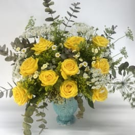 Yellow roses in a turquoise vase with airy white filler flowers