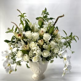 White roses and orchids arranged in a white urn vase