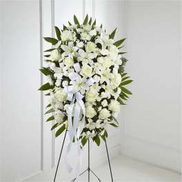 Tall standing spray of white lilies and roses with a white bow on a metal easel