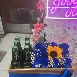 Blue roses and a sunflower in a wooden box with beer bottles