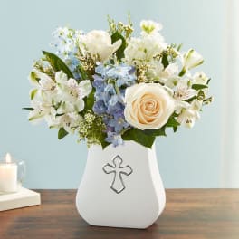 White and blue flower arrangement in a white vase with a cross