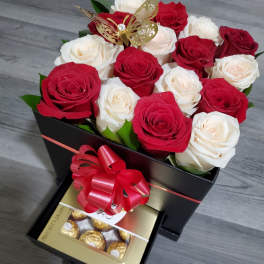 Red and white roses in a black gift box with chocolates and a ribbon