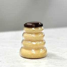 Beehive-shaped plastic jar filled with light golden contents and a dark brown lid on a light surface.