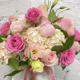 Pink roses and pale blooms arranged in a white vase with a ribbon