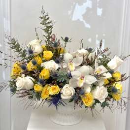 White and yellow roses with white orchids in a white pedestal vase
