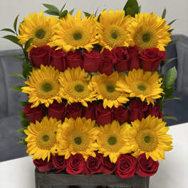 Sunflowers and red roses arranged in a wooden box with a pink ribbon