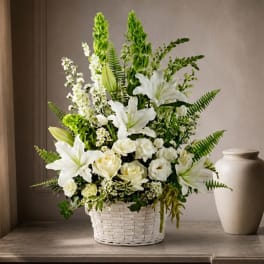 White lilies and roses arranged in a white basket with green accents