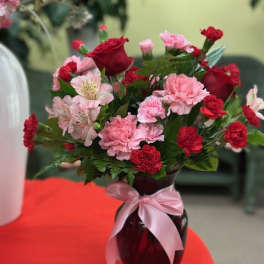 Bouquet of red roses and pink carnations in a dark vase with a pink ribbon