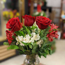 Red roses and white flowers arranged in a glass jar vase
