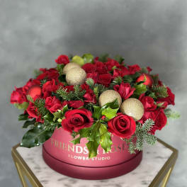 Red roses arranged in a pink round box with gold ornaments