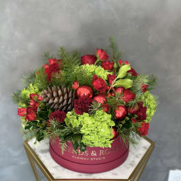 Red roses and green hydrangeas in a pink round box with pinecones and ornaments