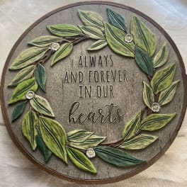 Round wooden wall sign with leafy wreath and the words "Always and Forever in Our Hearts"