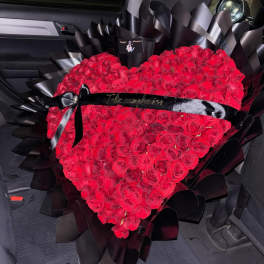 Heart-shaped bouquet of red roses wrapped in black paper with a black ribbon