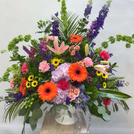 Large mixed flower arrangement in a white vase with orange gerberas and pink lilies