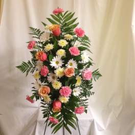 Tall floral standing arrangement with pink carnations, peach roses, and white daisies