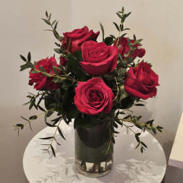 Red roses arranged in a clear glass vase with dark greenery