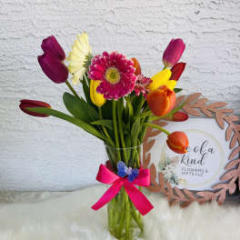 Colorful tulip and gerbera bouquet in a clear glass vase with a pink ribbon