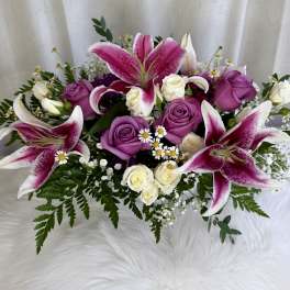 Pink lilies and purple roses arranged with small white flowers.