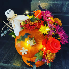 Pumpkin arrangement with colorful flowers, a ghost decoration, and bat accents