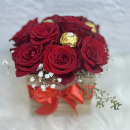 Red roses in a small box with a red ribbon and gold chocolates