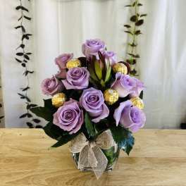 Lavender rose arrangement in a glass vase with gold-wrapped chocolates