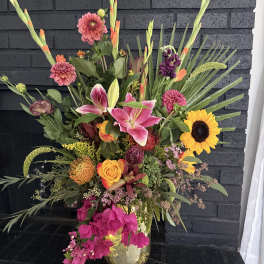 Tall mixed bouquet with lilies, roses, sunflowers, and pink blooms in a glass vase
