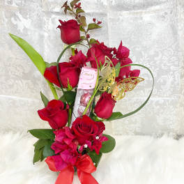 Red roses arranged with pink flowers, a ribbon, and a chocolate box
