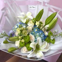 Bouquet of white lilies, blue hydrangeas, and cream roses wrapped in clear paper