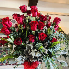 Red roses arranged in a clear glass vase with greenery and a red ribbon