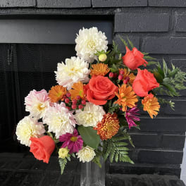 Mixed bouquet of red roses, white dahlias, and orange blooms in a clear vase