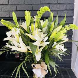 White lilies and green blooms in a glass vase with a burlap bow