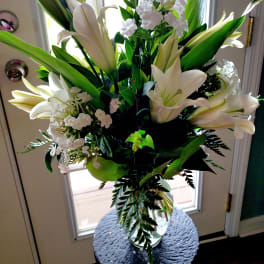 Tall bouquet of white lilies and small white flowers in a glass vase