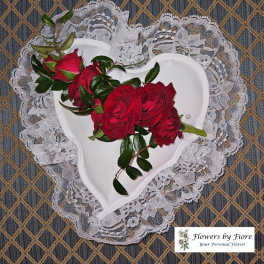 Red roses arranged in a white heart-shaped holder with lace trim