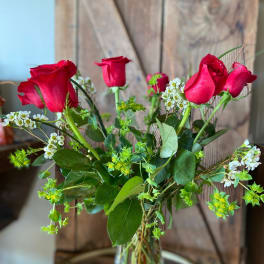 Tall arrangement of red roses and small white flowers in a clear glass vase