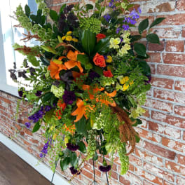 Tall standing spray with orange lilies, roses, purple delphinium and mixed blooms on a metal easel