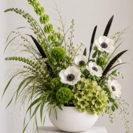 Green and white floral arrangement in a white bowl vase