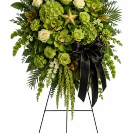Green floral standing spray with white roses and a black ribbon on an easel