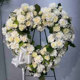 Heart-shaped white floral wreath on an easel with a silver bow