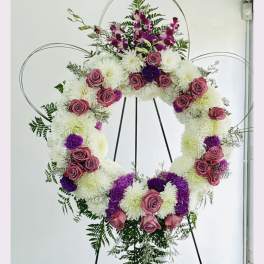 Large floral wreath on a stand with pink roses, white mums, and purple flowers