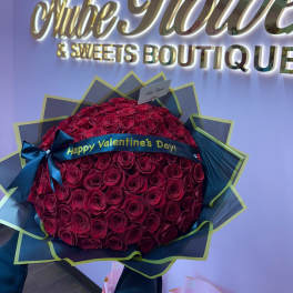 Large bouquet of red roses wrapped in dark paper with a Valentine ribbon