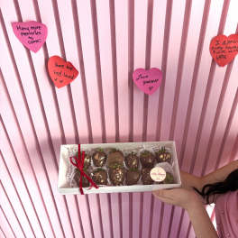 Box of chocolate-covered strawberries held in front of pink heart notes