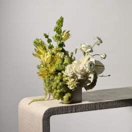 White and green floral arrangement in a vase with grapes and an apple