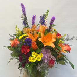 Colorful mixed bouquet in a glass vase with orange lilies and purple flowers