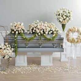 Set of ivory and peach rose funeral arrangements around a gray casket with greenery garlands.