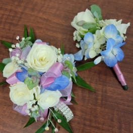 Two small floral bouquets with white roses and blue hydrangea accents on a wooden surface.
