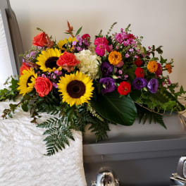 Bright mixed flower spray on a casket with sunflowers, roses, and purple blooms