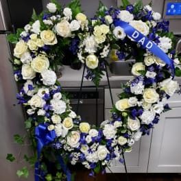Heart-shaped floral wreath with white roses and blue flowers on a stand