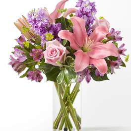 Pink lilies and roses with purple flowers in a clear glass vase
