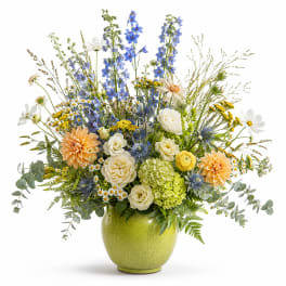 Mixed bouquet in a green vase with blue, white, yellow, and peach flowers